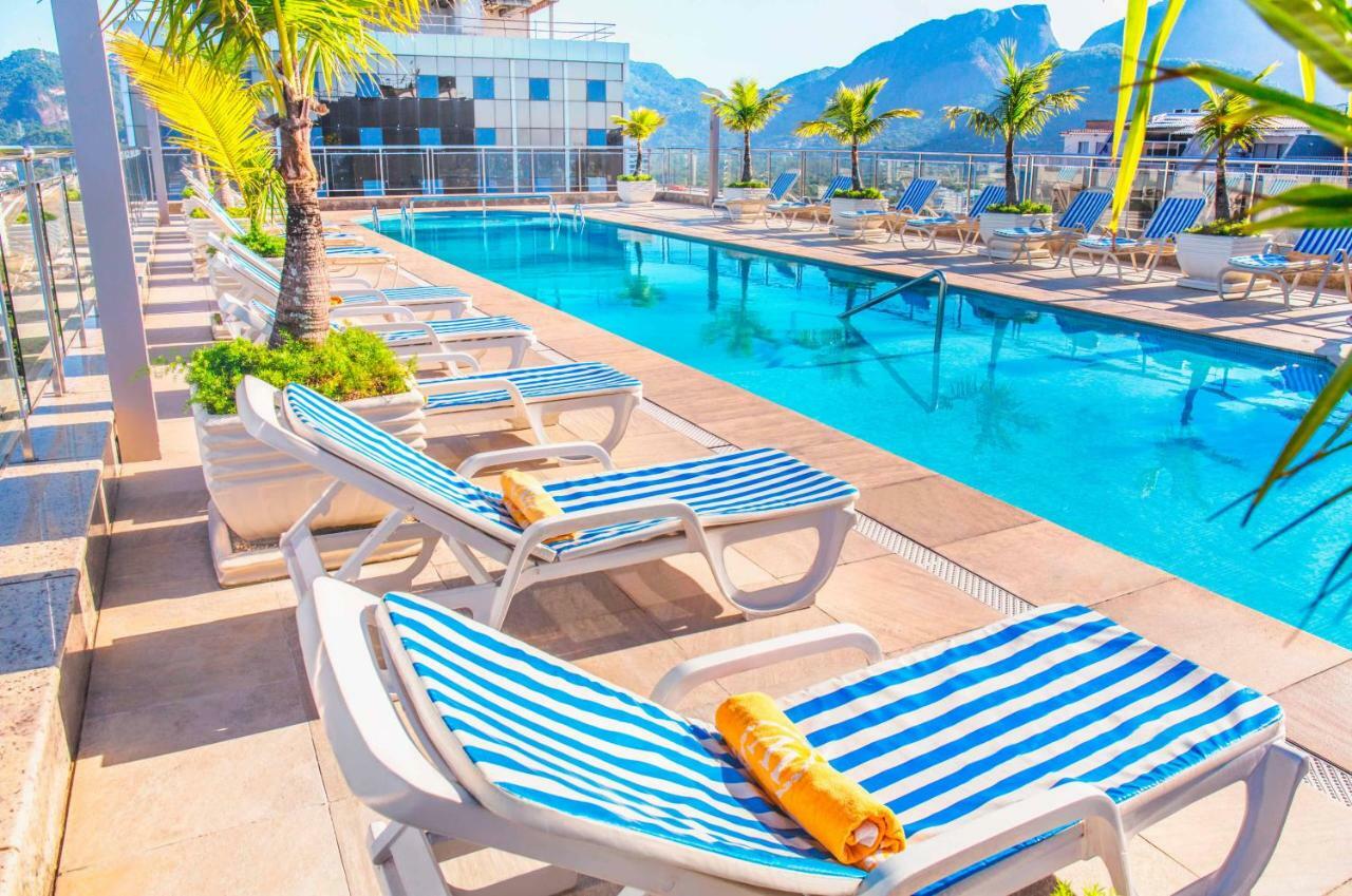 Windsor Barra Hotel Rio de Janeiro Esterno foto The photo shows a vibrant outdoor swimming pool area. There are several lounge chairs with blue and white striped cushions arranged around the pool. Some of the chairs have towels placed on them. In the background, the pool is clear and reflects the 